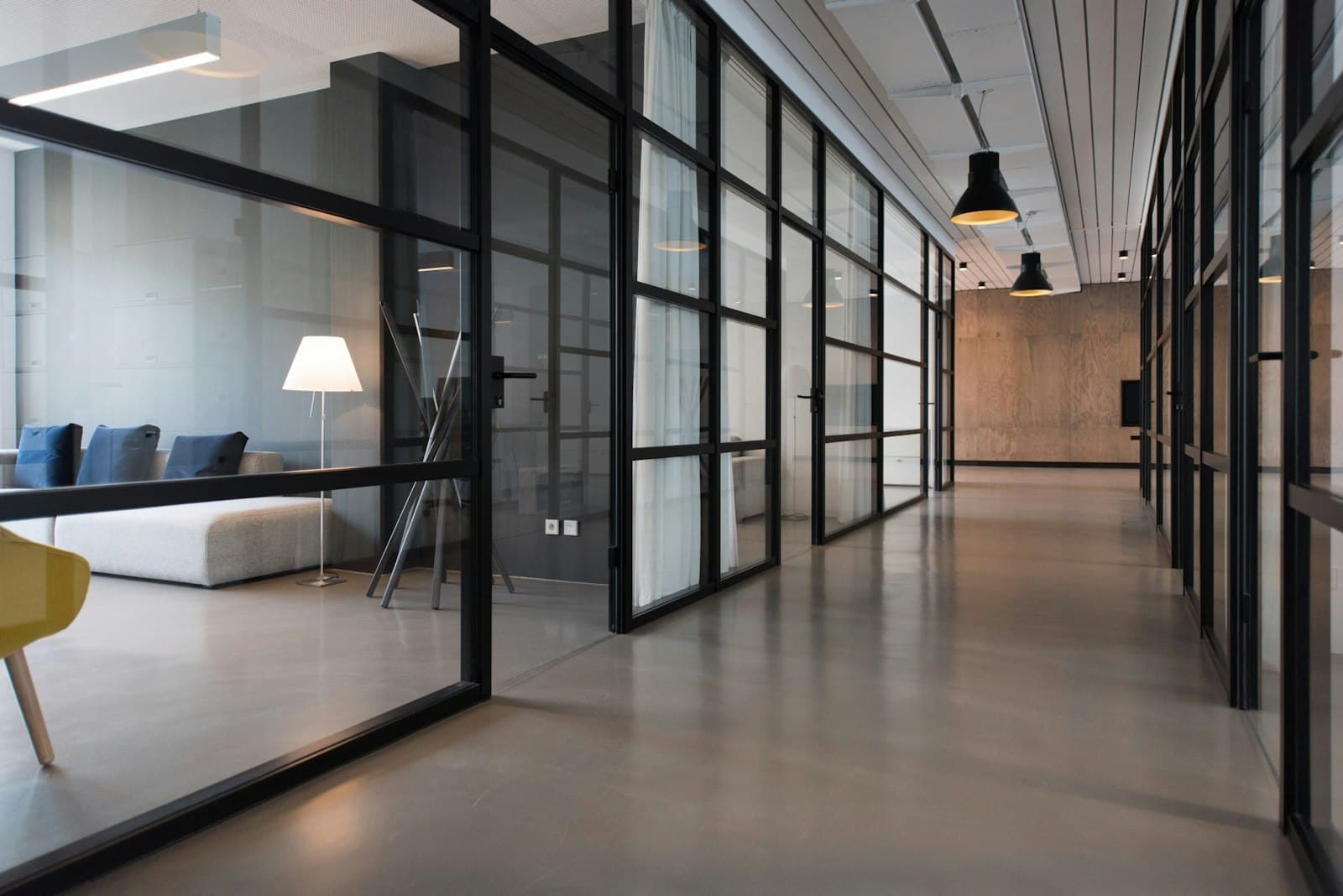 A glass-lined corridor with a waiting sofa visible beyond black frames.
